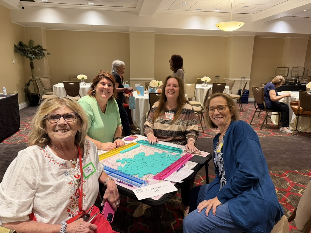 Four guests smiling together around a Mah Jongg table